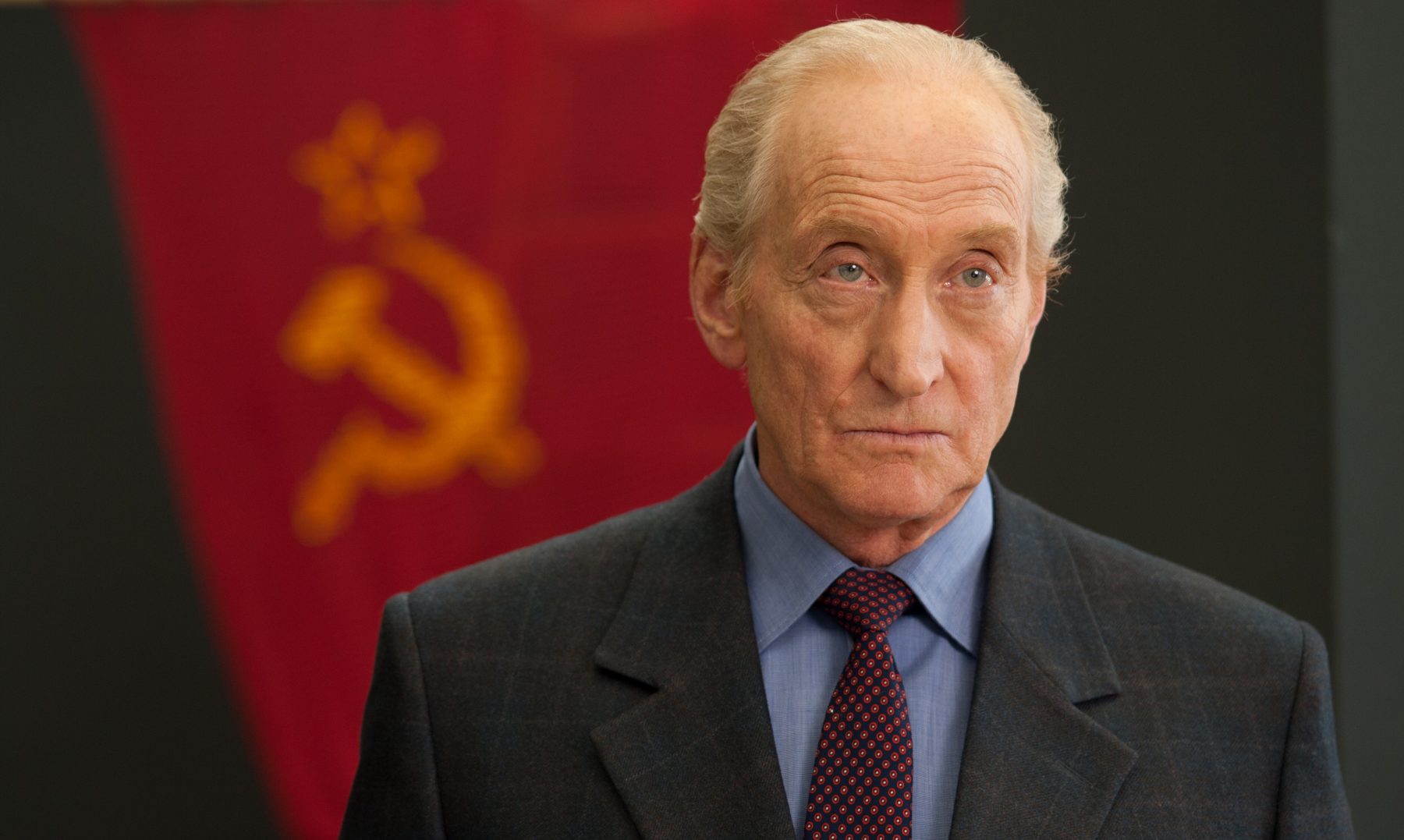 A man in a suit and tie standing in front of a communist flag.